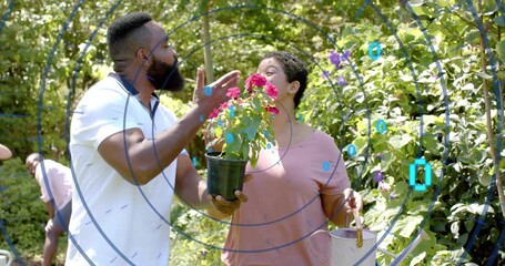 Man pointing at bloom, woman leaning in inspecting plant in garden, HUD highlighting care tips