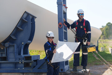 Fototapeta premium Engineers in safety gear conduct a detailed inspection of wind turbine blades at a construction site. Large blades are placed on the ground, highlighting the renewable energy technology.