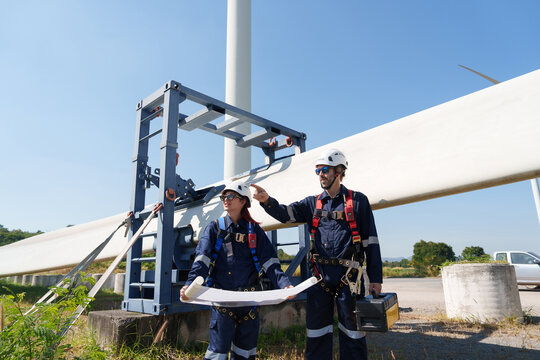 Engineers in safety gear conduct a detailed inspection of wind turbine blades at a construction site. Large blades are placed on the ground, highlighting the renewable energy technology.