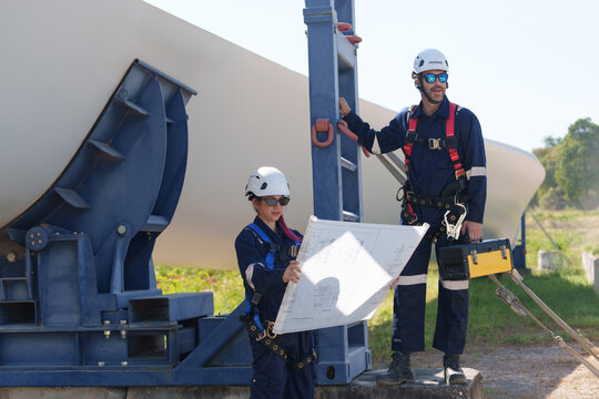 Engineers in safety gear conduct a detailed inspection of wind turbine blades at a construction site. Large blades are placed on the ground, highlighting the renewable energy technology.