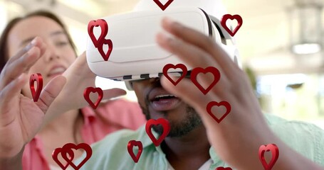 Man putting on VR headset while woman adjusting, 3D hearts appearing, he reaching to interact