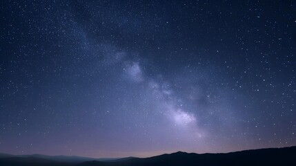 Fototapeta premium The majestic Milky Way galaxy arches across a dark star filled night sky above silhouetted mountains