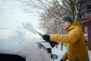 Man in winter clothing clearing snow from car parked in residential city street during cold...