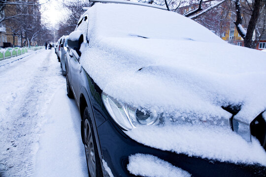 Snow-covered cars parked on a quiet residential street during a winter day in a charming neighborhood