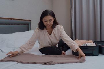 Asian woman packing and folding clothes into suitcase for travel in Europe