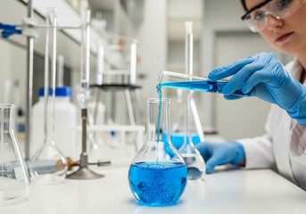 Female Scientist Carefully Pouring Blue Liquid from a Test Tube into a Glass Flask in a Laboratory