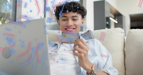 Man on couch holding card and checking laptop, causing animated confetti confirming fintech payment - Powered by Adobe