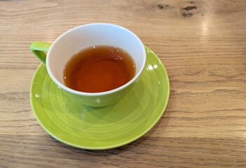 木製テーブルの上に置かれたライムグリーンのカップソーサーと紅茶