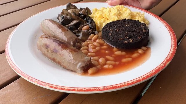 Serving a British Breakfast of Scrambled Eggs, Baked Beans, Blood Pudding and Sausages