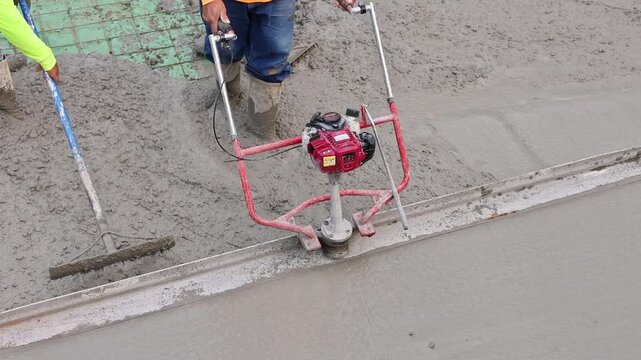 Worker operates concrete vibrator to create smooth finish on wet cement in construction area.