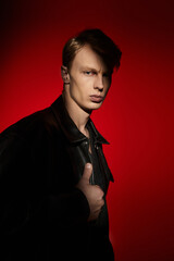 Young man embodies modern masculinity with striking pose against bold red backdrop