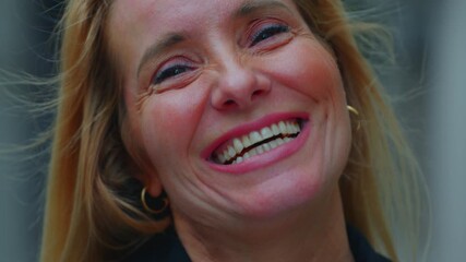 Close-up portrait of middle-aged woman smiling brightly with genuine joy, eyes crinkled and expression radiating warmth and confidence outdoors
