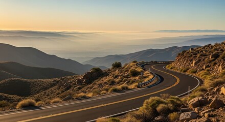 Winding mountain road at sunrise, with layers of misty hills and valleys stretching into the distance under a clear sky
