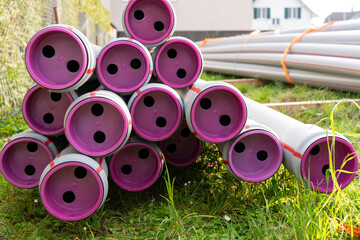 Stack of plastic pipes with violet end protection caps on the ground of a construction site.