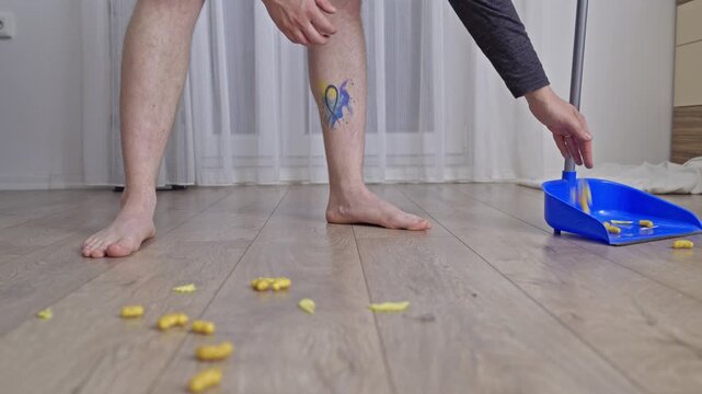 Person carefully collecting spilled snacks and chips from a wooden floor using their bare hands and a blue dustpan. This video captures a common household cleaning task.