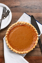 A fresh baked Pumpkin pie with server, plates and forks. The dessert is part of a typical...