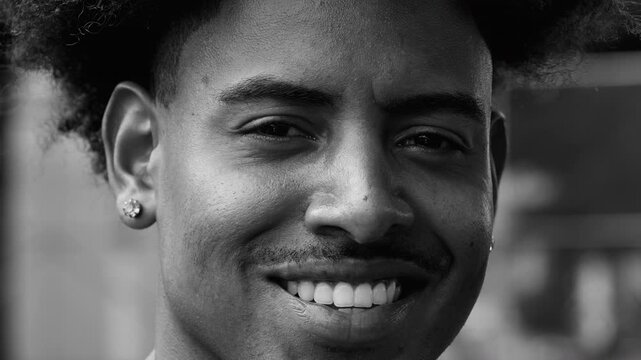Close-up portrait of young African American man smiling warmly, relaxed expression and confident presence conveying optimism and friendliness, in black and white