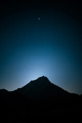 Mountain ridge silhouette beneath dark sky with one luminous star and faint haze