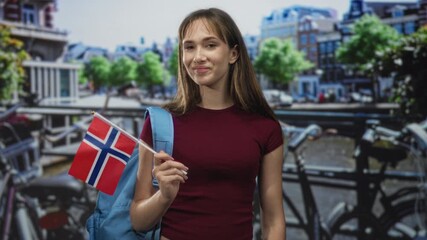 Student woman holding norwegian flag with her hand on a street bridge in amsterdam; pride travel youth.