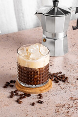 Iced creamy coffee into a glass with moka pot on beige kitchen table background. Coffee break during a hot summer day, refreshing drink