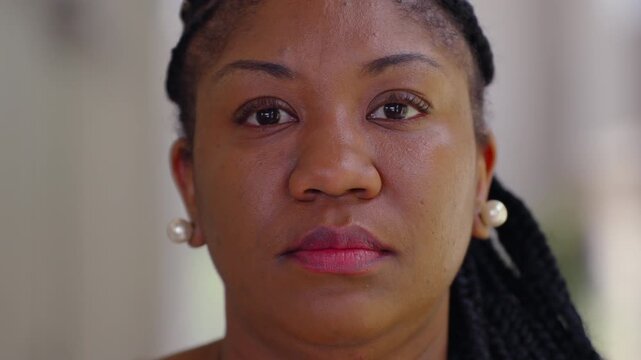 Portrait of African American woman looking directly at camera with calm steady expression, natural light highlighting her face and braided hair against soft blurred background - Powered by Adobe