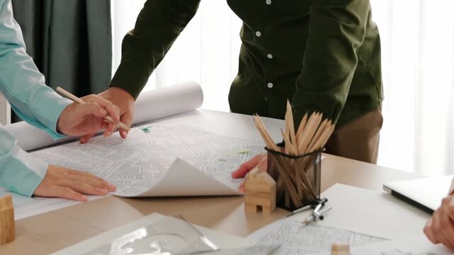 Smart architect and safety engineer discussion about building blueprint on table with architectural document, measurement tools and wooden block scatter around at modern office. Closeup. Delineation.