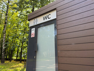 The entrance door to modern outdoor restroom, finished with wooden blocks and dual gender indicators. Shared stall in public restroom for the convenience of people in the park