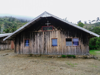 A rustic wooden church standing in a remote mountain village, featuring weathered timber walls, a cross on the roof, and a serene natural backdrop. Perfect for themes of faith, tradition, and rural li