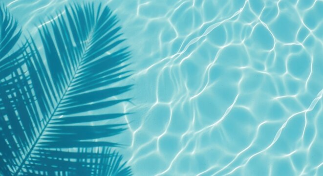 Closeup of clear turquoise swimming pool water with gentle ripples and sunlight creating abstract patterns, featuring the shadow of a palm leaf