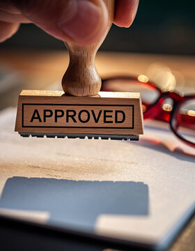 Hand holding wooden stamp with APROVED text over document approved rubber stamp