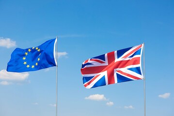 The european union flag and the union jack flag of the united kingdom waving together against a clear blue sky with white clouds