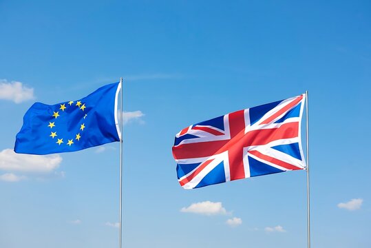 The european union flag and the union jack flag of the united kingdom waving together against a clear blue sky with white clouds - Powered by Adobe