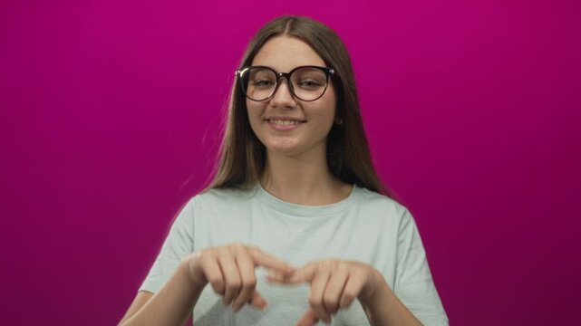 Caucasian teenage girl puckers lips and closes eyes in a studio with a bright pink backdrop; playfulness.