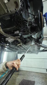 Technician in protective suit powerwashing undercarriage with high pressure lance, dramatic spray and runoff, focus on safety suit, gloves and heavy duty cleaning in professional bay