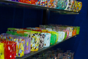 Colorful Murano glass fills the shelves in vibrant rows. Patterns swirl across each handmade vessel in Venice, Italy. Bright tones create a lively harmony in this artisan display.