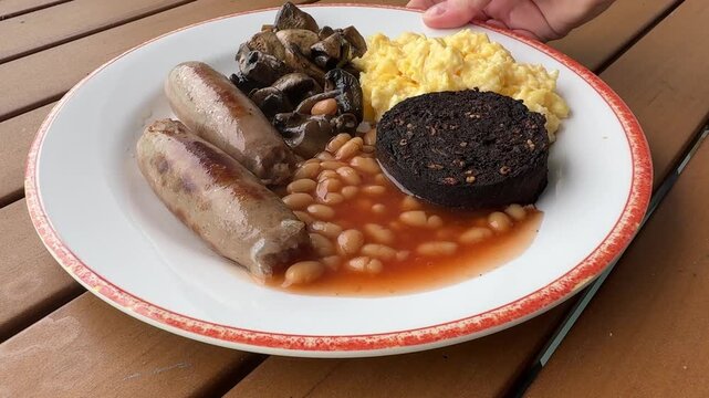 Serving a British Breakfast of Scrambled Eggs, Baked Beans, Blood Pudding and Sausages 