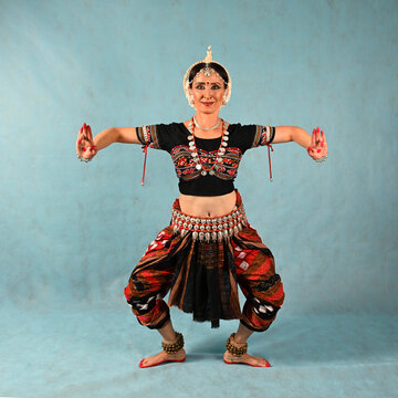 An Indian dancer girl poses in a dance pose in a studio on a blue background