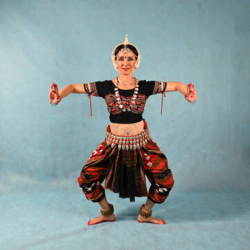 An Indian dancer girl poses in a dance pose in a studio on a blue background
