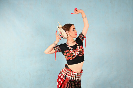 An Indian dancer girl poses in a dance pose in a studio on a blue background