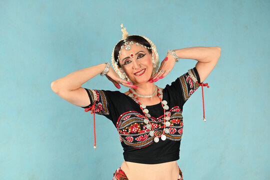 An Indian dancer girl poses in a dance pose in a studio on a blue background