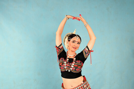 An Indian dancer girl poses in a dance pose in a studio on a blue background