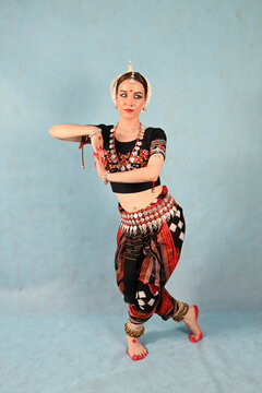 An Indian dancer girl poses in a dance pose in a studio on a blue background
