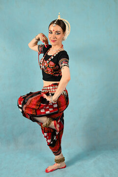 An Indian dancer girl poses in a dance pose in a studio on a blue background