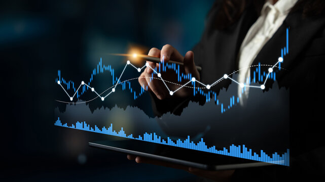 A business professional reviews financial data using a tablet while interacting with digital stock market graphs, emphasizing analysis and strategy in a sophisticated office environment. Scalp
