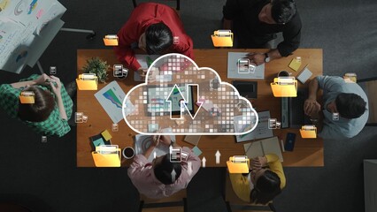 A group of diverse professionals collaborates around a table, sharing ideas and discussing strategies while symbols of cloud storage and file sharing enhance the workspace. Raster