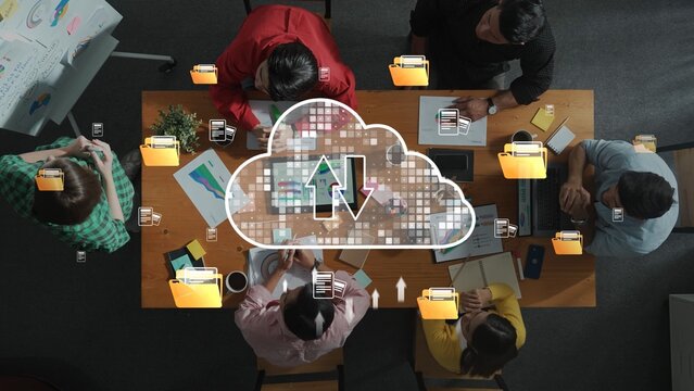 A group of diverse professionals collaborates around a table, sharing ideas and discussing strategies while symbols of cloud storage and file sharing enhance the workspace. Raster