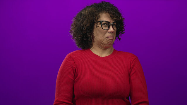 Middle aged woman with curly hair and glasses with palms outward blocking gesture in purple studio; rejection.