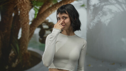 Young hispanic woman wearing white crop top points finger at camera in building courtyard; confidence empowerment.