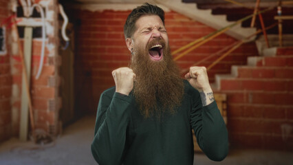 Bearded man energetically pumping fists in unfinished building space with exposed brick and...