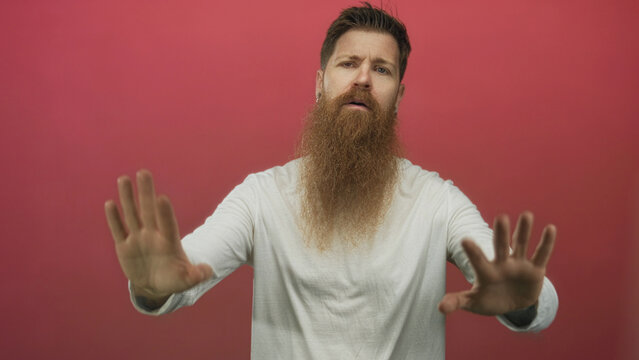 Man with long beard wearing white shirt pushes both palms forward toward camera in studio setting; resistance.